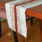 beige colored embroidered table runner with red patch in center and golden embroidery and tassels on corners for 6 seater table - 52x84 inches.