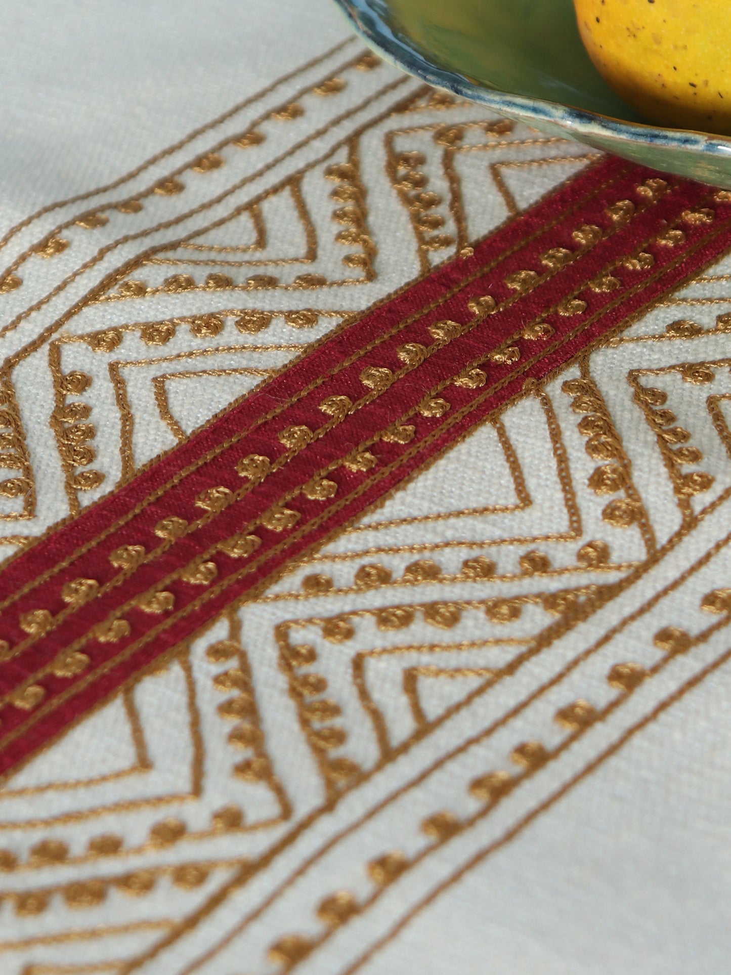 closeup of embroidery on beige colored table runner with red patch in center and golden embroidery and tassels on corners for 6 seater table - 52x84 inches.