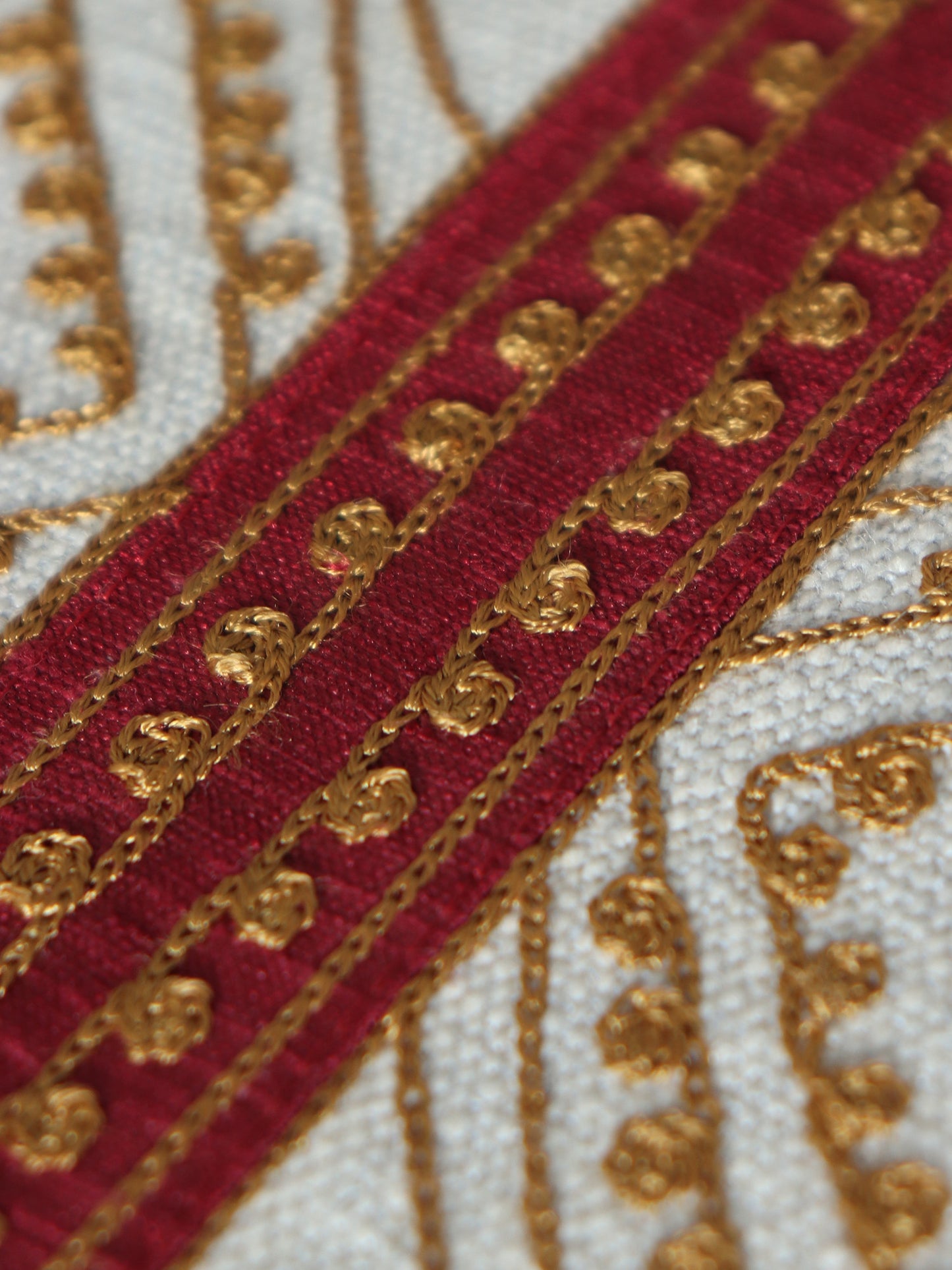 closeup of embroidery on beige colored table runner with red patch in center and golden embroidery and tassels on corners for 6 seater table - 52x84 inches.