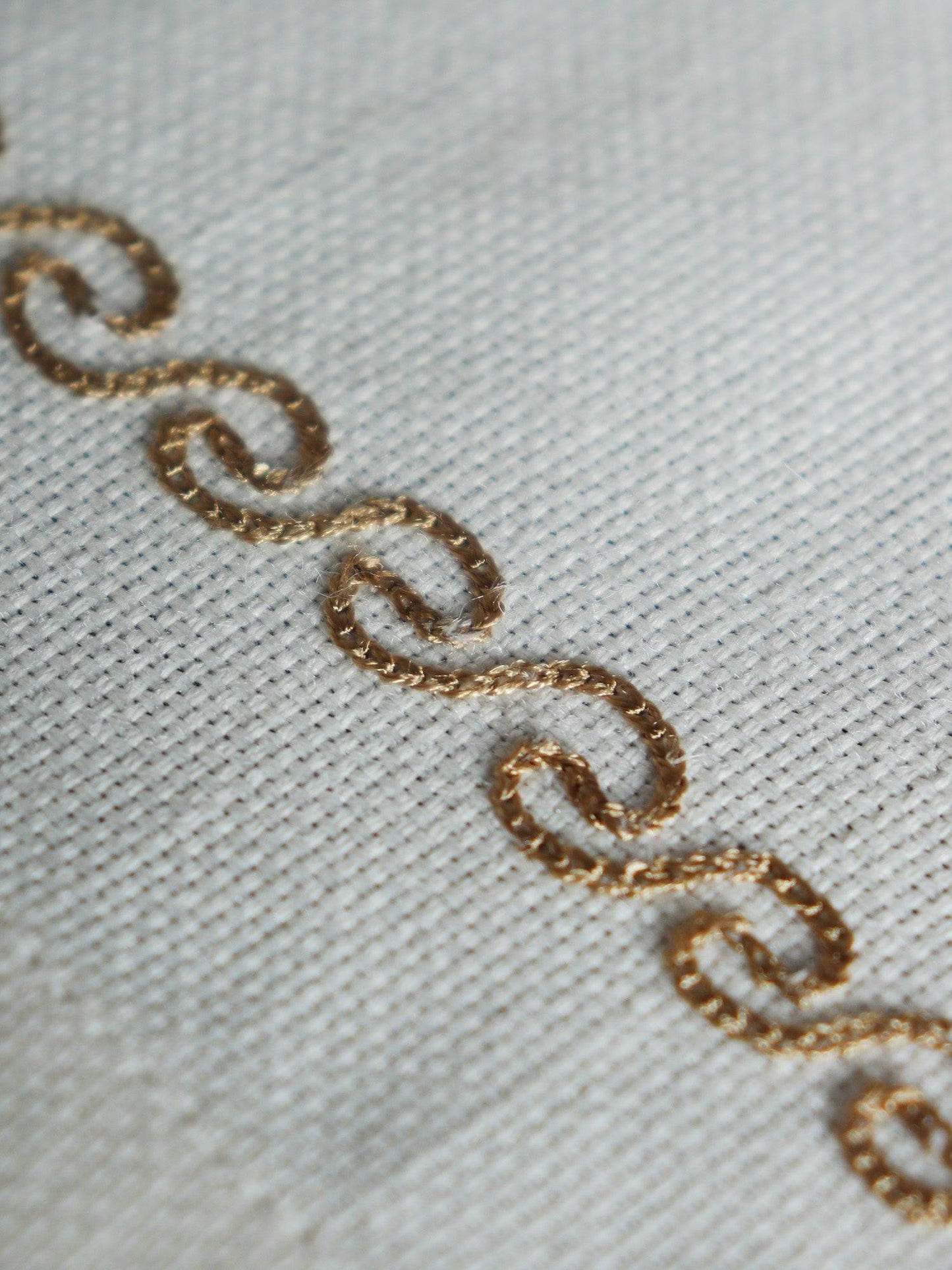 wavy patterned embroidery in golden color on an offwhite table runner