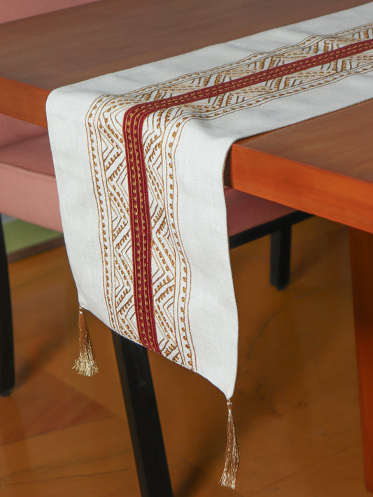 beige colored embroidered table runner with red patch in center and golden embroidery and tassels on corners for 6 seater table - 52x84 inches.
