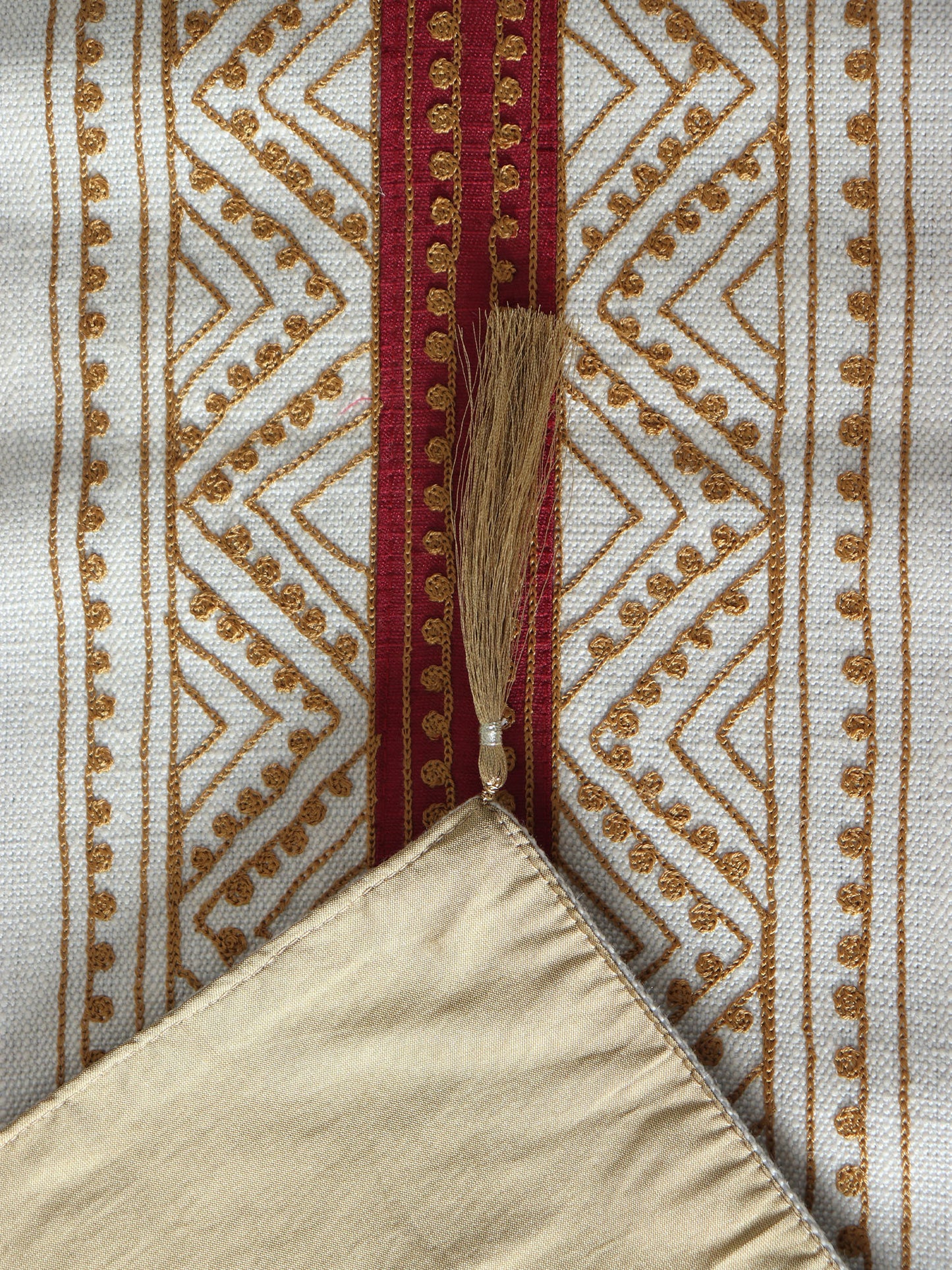 closeup of embroidery on beige colored table runner with red patch in center and golden embroidery and tassels on corners for 6 seater table - 52x84 inches.